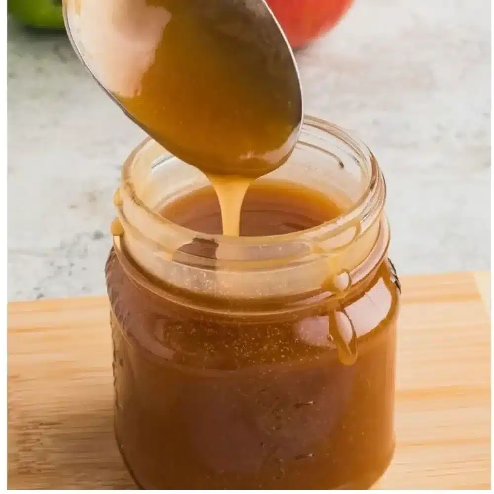Homemade caramel sauce in a jar with a spoon and dessert drizzled with caramel