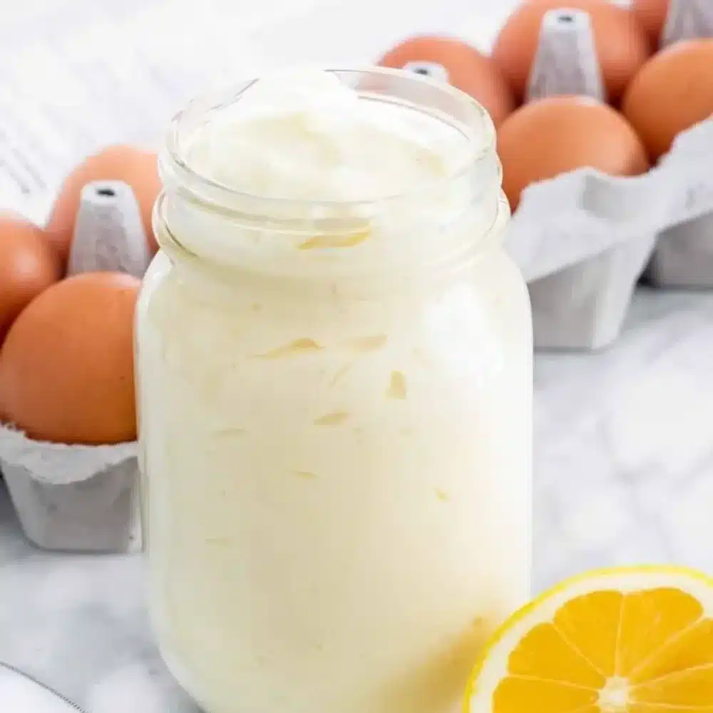 A jar of homemade Dukes Mayo with fresh ingredients surrounding it.