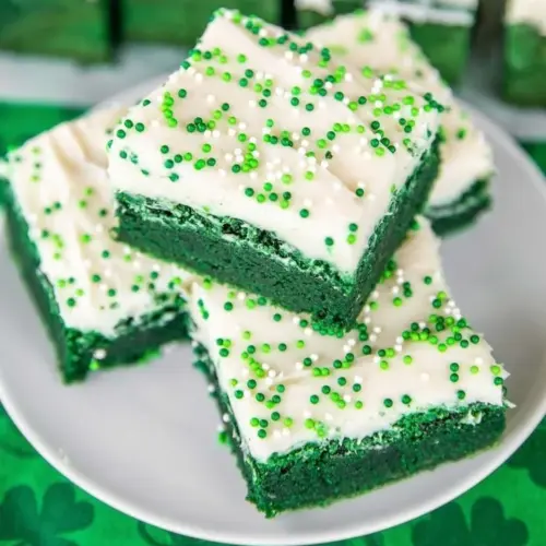 Delicious green velvet brownies topped with cream cheese frosting on a plate.