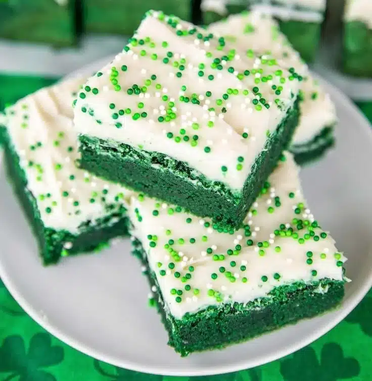 Delicious green velvet brownies topped with cream cheese frosting on a plate.