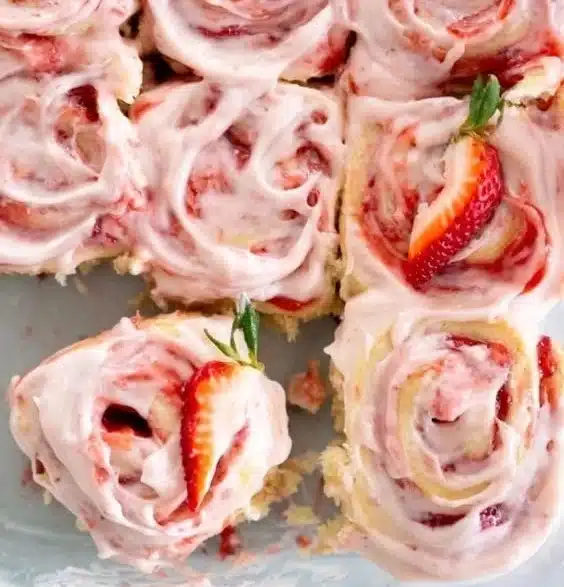 Freshly baked strawberry cinnamon rolls topped with icing and strawberries
