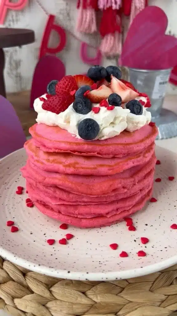Stack of heart-shaped Valentine's Day pancakes with strawberries and syrup
