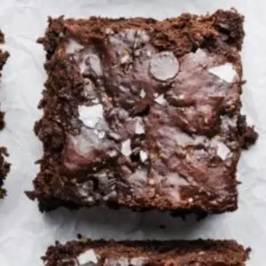 Fudgy zucchini brownies topped with chocolate drizzle on a white plate