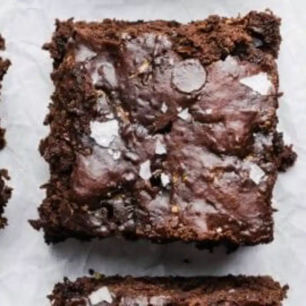 Fudgy zucchini brownies topped with chocolate drizzle on a white plate
